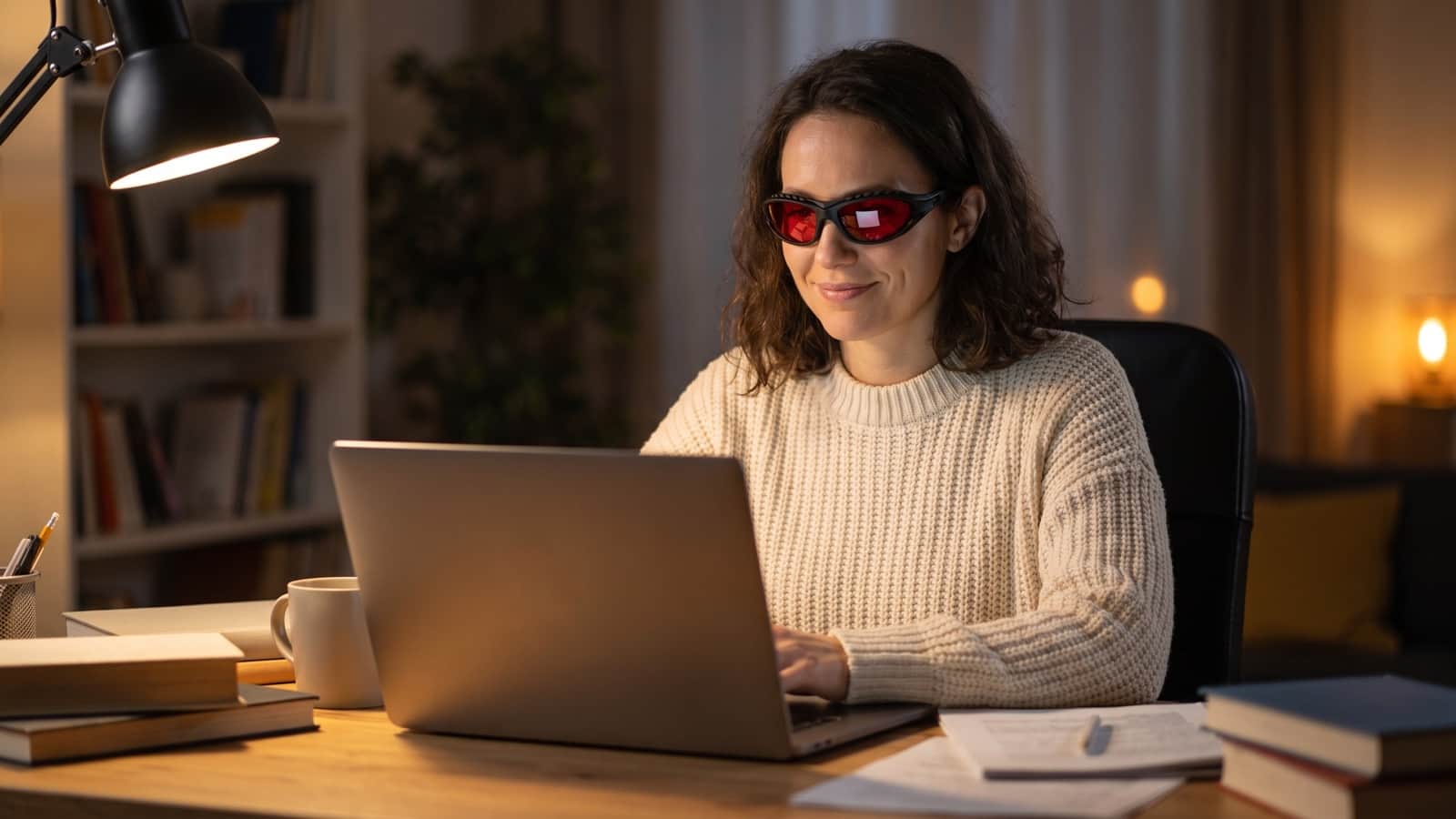 Femme portant des lunettes anti-lumière bleue teintées devant son ordinateur portable dans la lumière chaude du soir