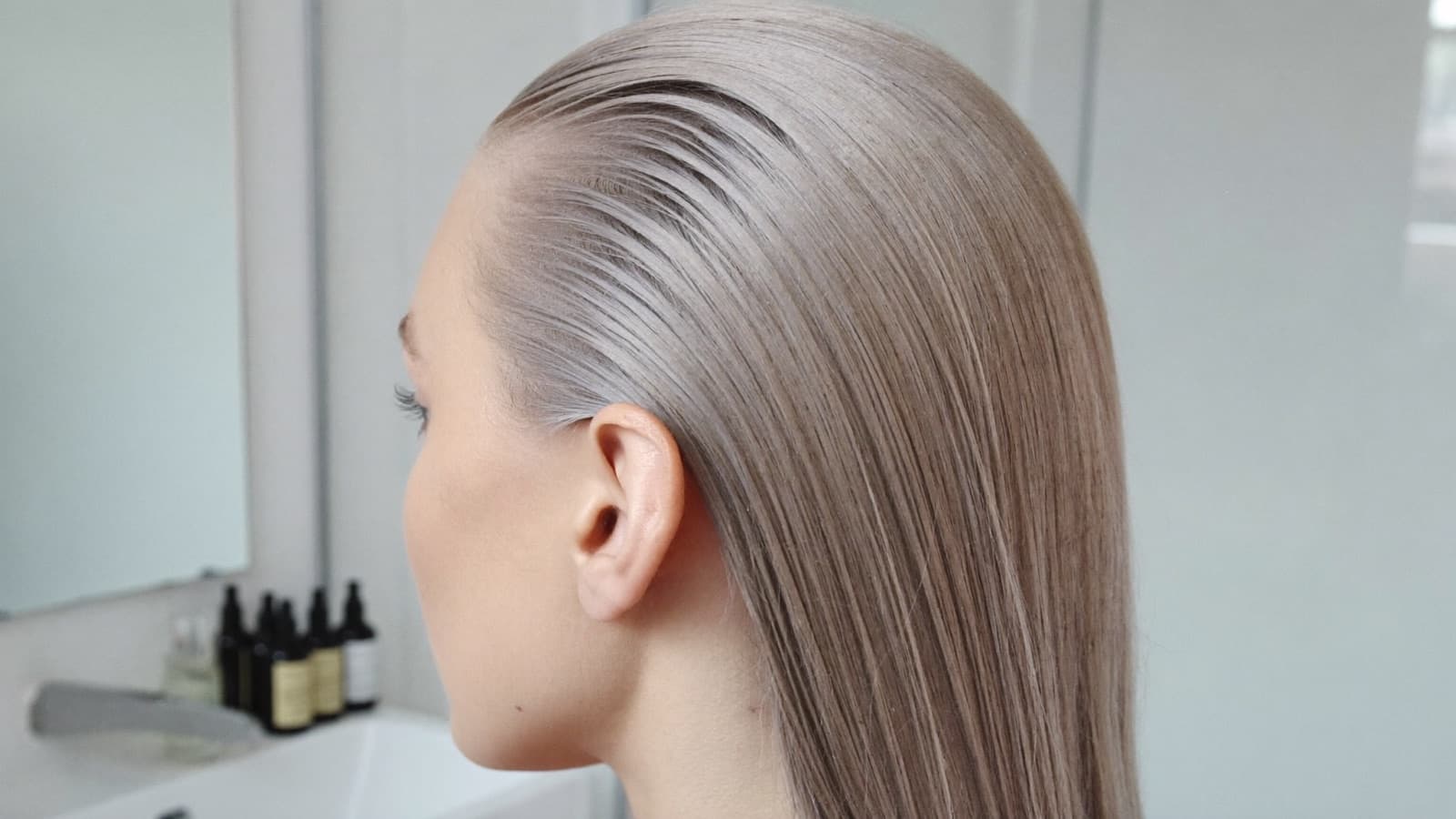 Frau mit kühlem Aschblond in einem hellen, minimalistischen Badezimmer