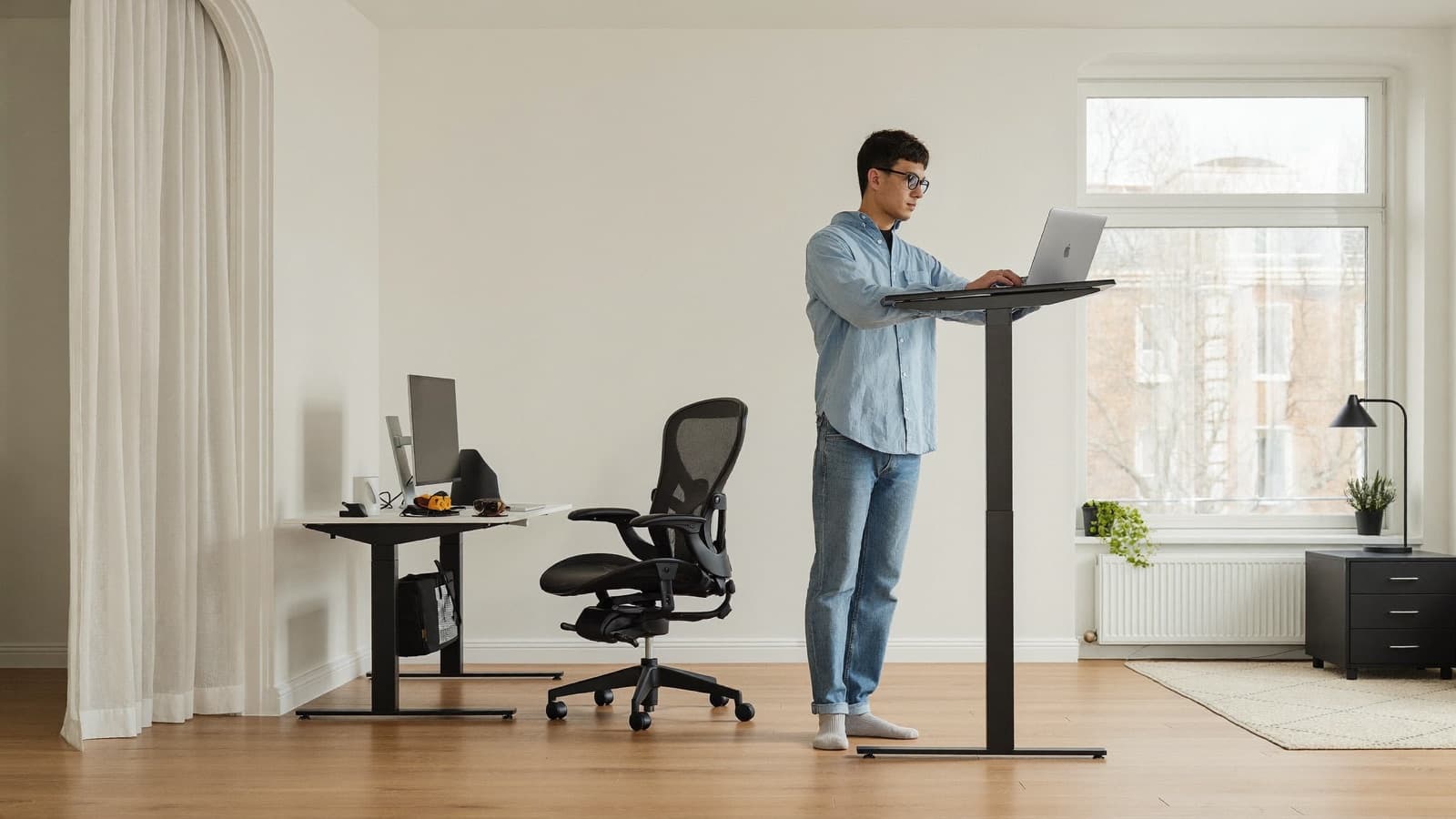 Person arbeitet im Stehen an einem höhenverstellbaren Schreibtisch im hellen Homeoffice
