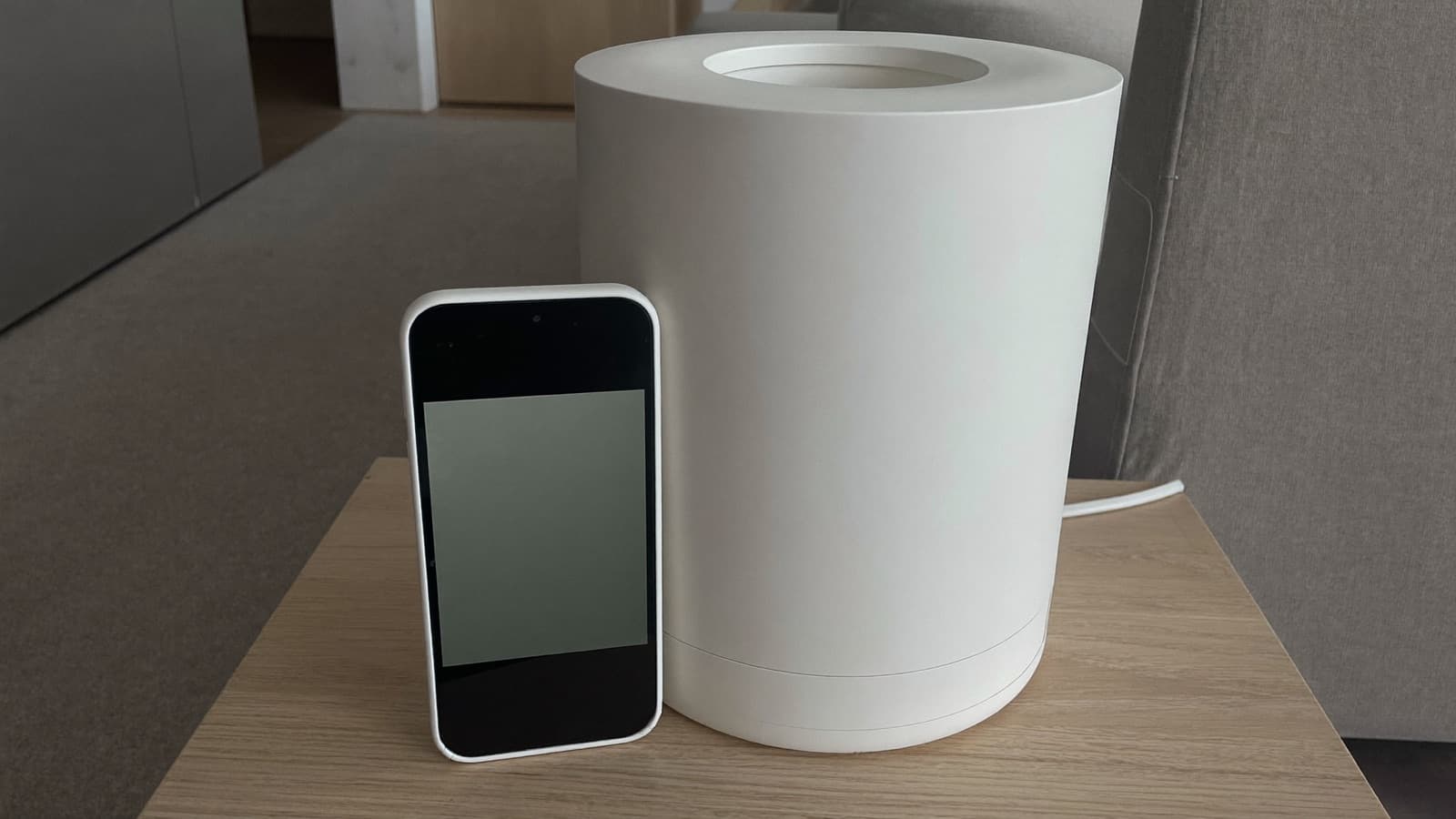 Smartphone and a small white device on a side table in a calm, modern living room